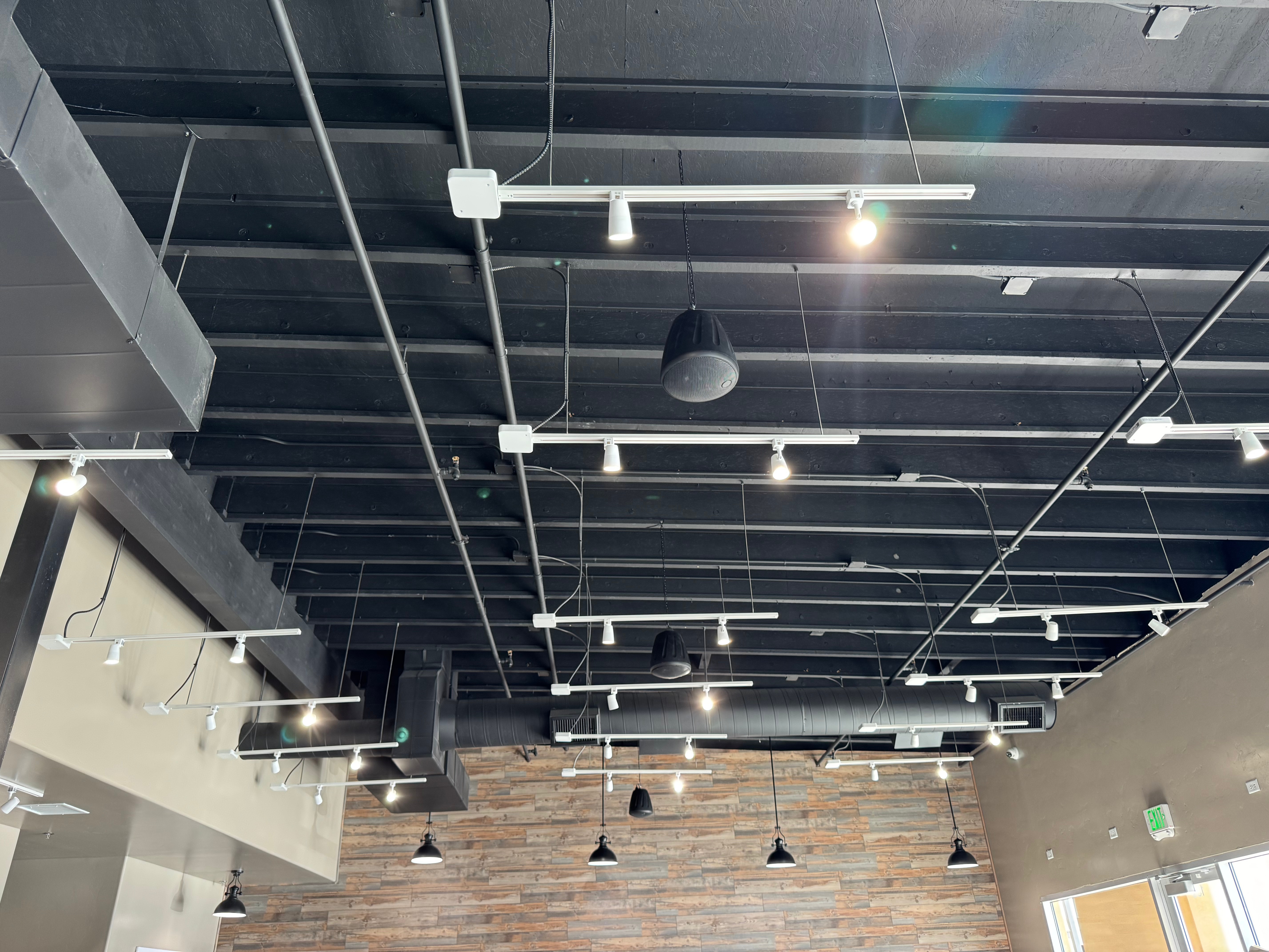 Interior view of a modern space featuring a black ceiling with various track lights and pendant lamps, complemented by a wooden accent wall.